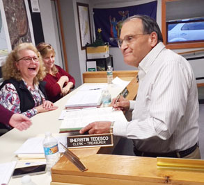 man signs book with woman laughing in front of him