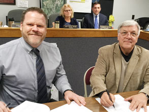 two men sign papers together
